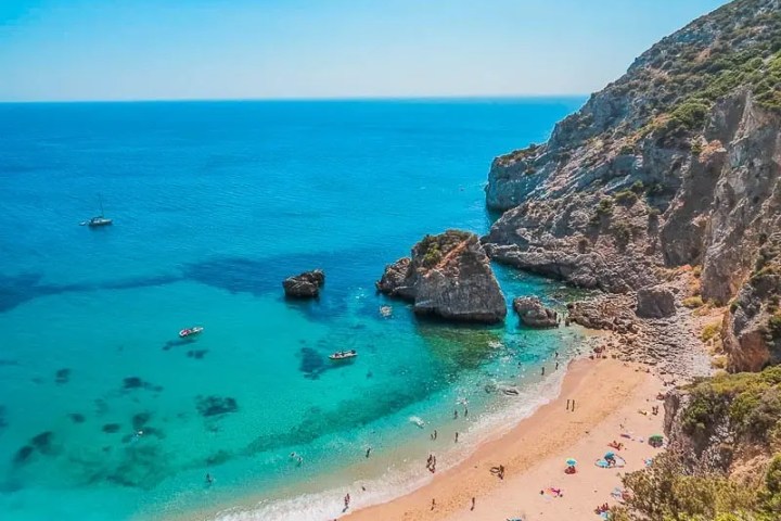 Scenic beach with turquoise water, rocky cliffs, and sunbathers.