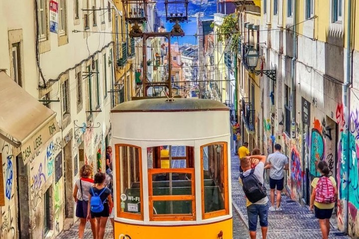 Yellow tram on steep street with colorful buildings and people walking.
